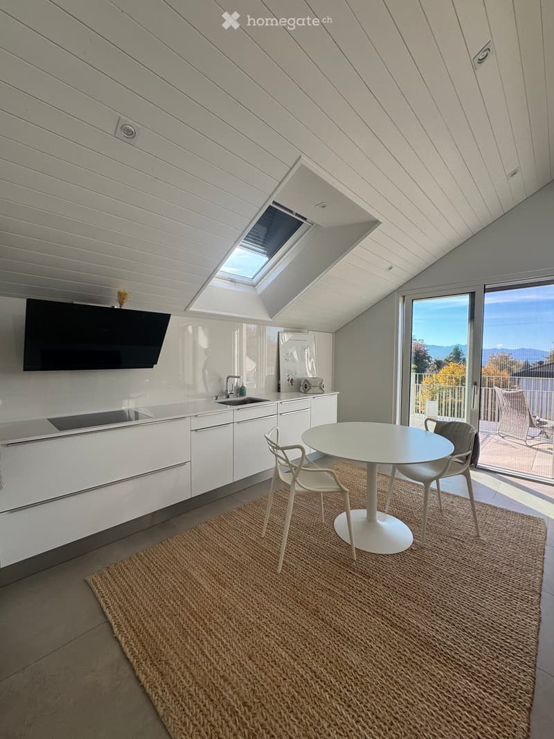 Modern kitchen with white cabinets, a round dining table with chairs, a sink, and a large window offering a scenic view.