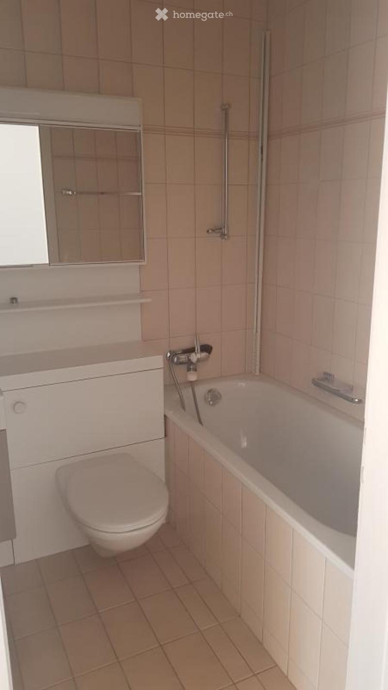 Modern bathroom with a white toilet, bathtub, mirror cabinet, and tiled walls and floor.