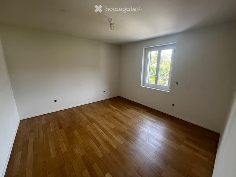 Empty room with wooden flooring and white walls, featuring a single window with white frame and visible outdoor view.
