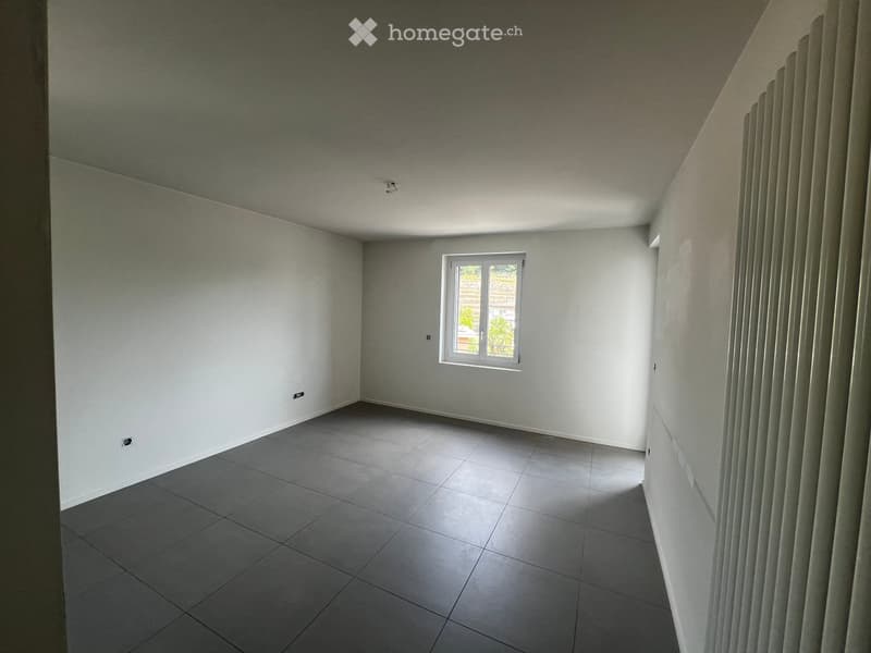 Empty room with grey tiled floor, white walls, and a single window with white frame. No furniture or equipment visible.