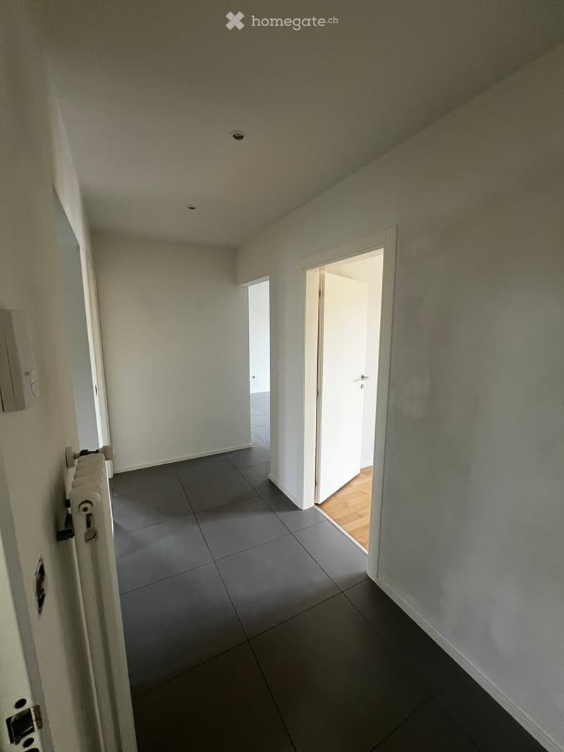 Empty hallway with grey tiled floor, white walls, and two open doors leading to other rooms.