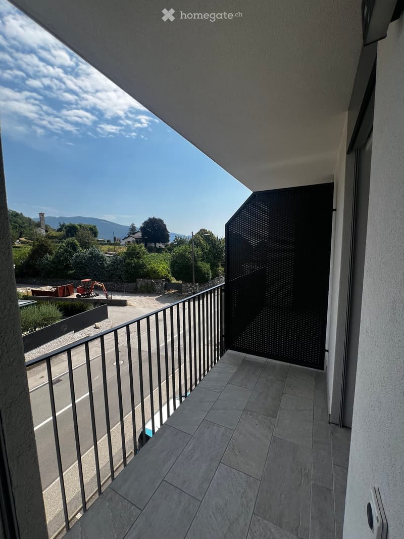 Balcony with tiled floor, metal railing, and a view of a road, trees, and distant mountains.