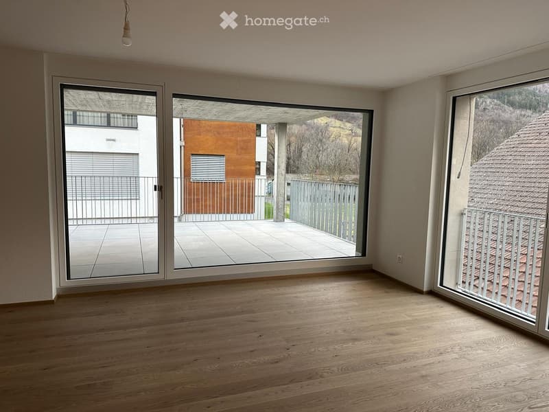 Empty room with wooden flooring, large sliding glass doors leading to a balcony, and a view of the surrounding area.