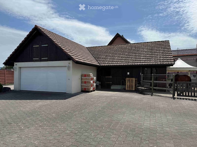 A two-part building with a garage and stable, featuring a tiled roof, white garage door, and a fenced area with a horse visible.