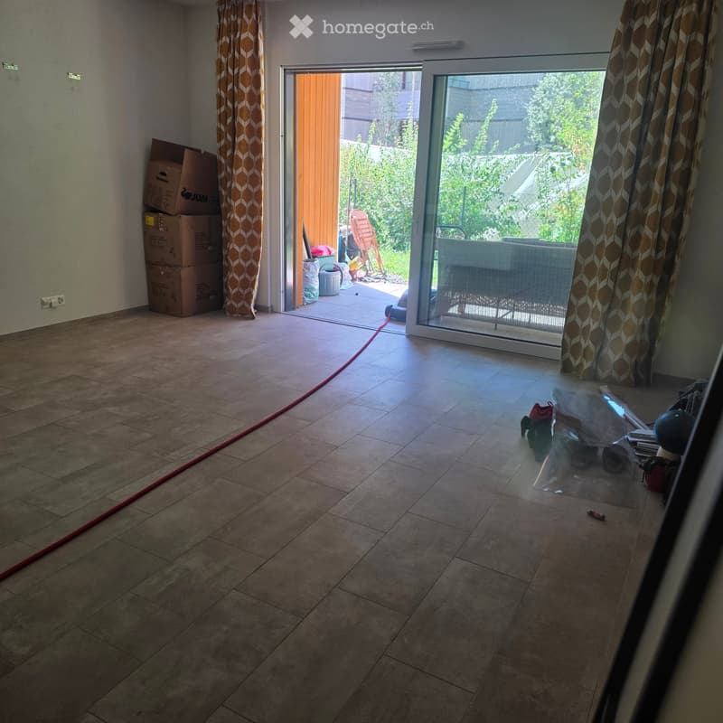 Empty room with tiled floor, large sliding glass door leading to outdoor area, stacked boxes, and a few scattered items near the entrance.