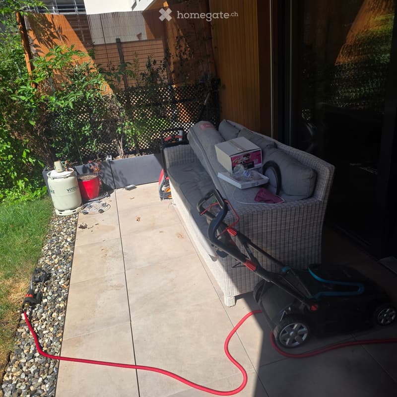 Garden area with a wicker sofa, lawn mower, garden hose, barrel, and bucket.