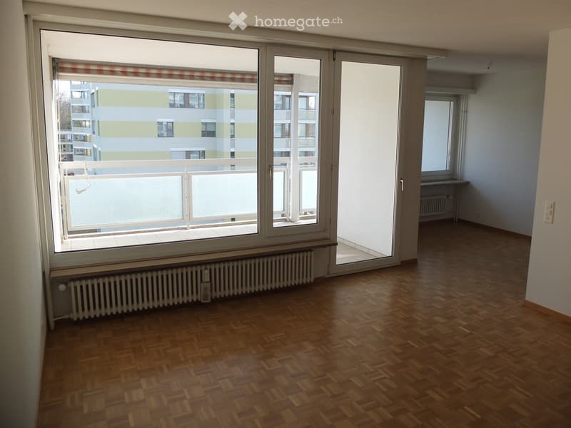Empty room with wooden flooring, large windows, radiator, and sliding glass door leading to a balcony.