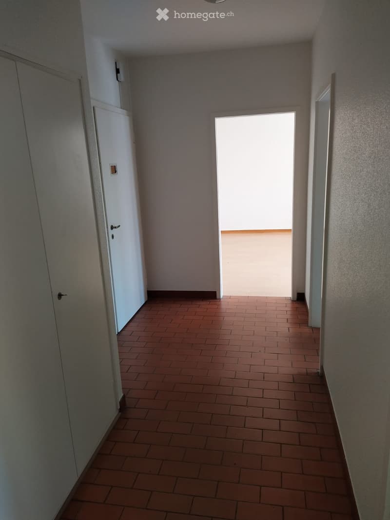 Empty hallway with tiled floor, white walls, and a door leading to a bright area.