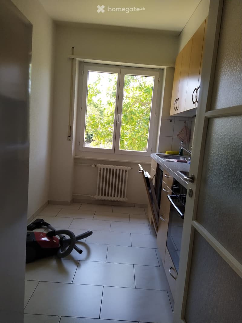 Empty kitchen with tiled floor, white cabinets, sink, oven, and a vacuum cleaner on the floor.