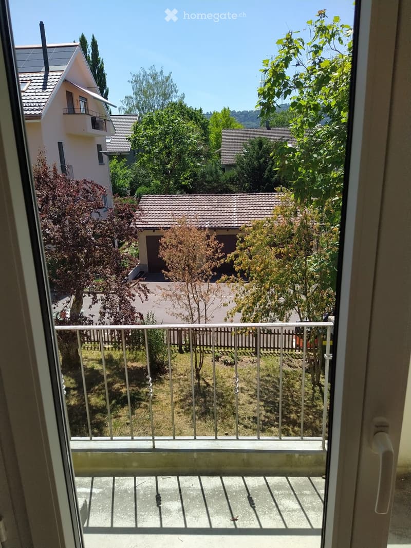 Balcony with metal railing overlooking a residential area with houses, trees, and a clear blue sky.