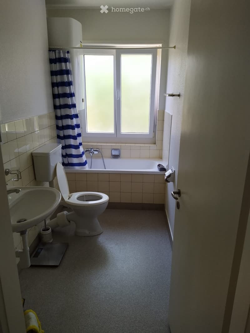Bathroom with a toilet, sink, bathtub, and window with a blue and white striped curtain.