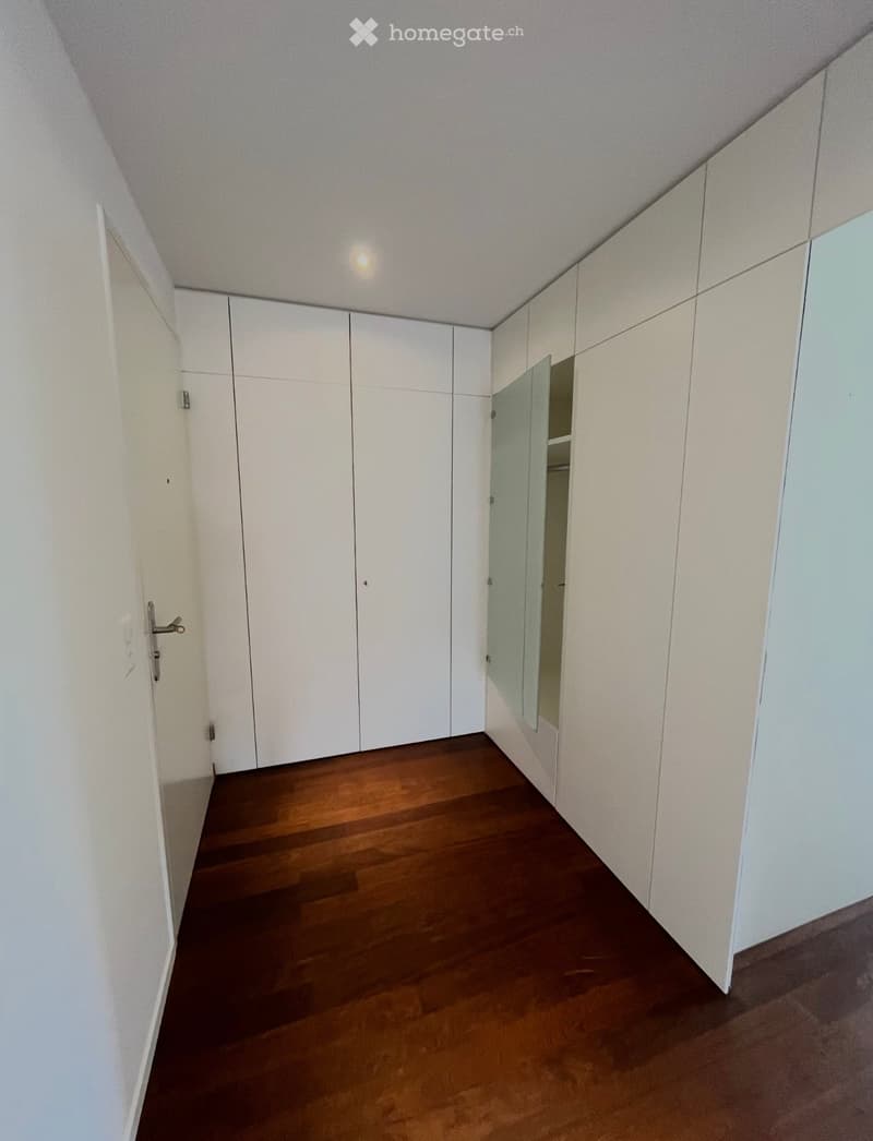 Empty room with white walls, wooden floor, and built-in white closet units.