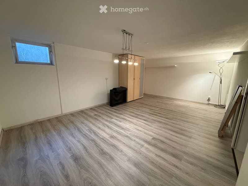 Empty room with light-colored walls, wooden flooring, and a single window. Contains a built-in wardrobe and a floor lamp, but no furniture.