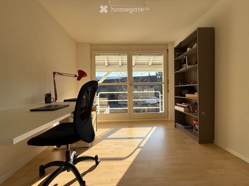 Bright, modern office with wooden flooring, large window, ergonomic chair, desk, and shelving unit.