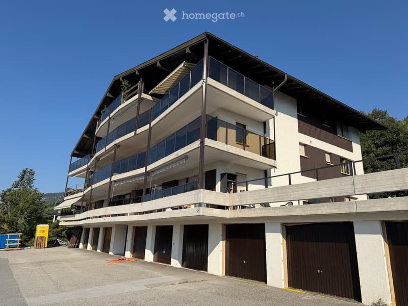 Modern multi-story building with balconies, large windows, and multiple garage doors on the ground floor.