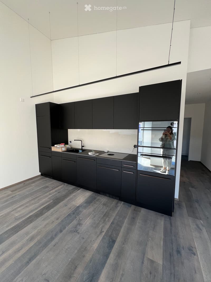 Modern kitchen with dark grey cabinets, a stainless steel sink, and a stove, featuring a light grey backsplash and wooden flooring.