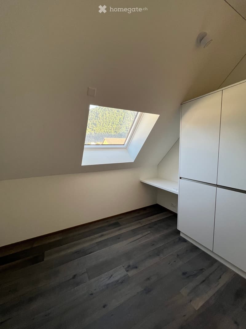 Empty room with wooden flooring, white cabinetry, and a skylight window offering a view of trees and a house outside.