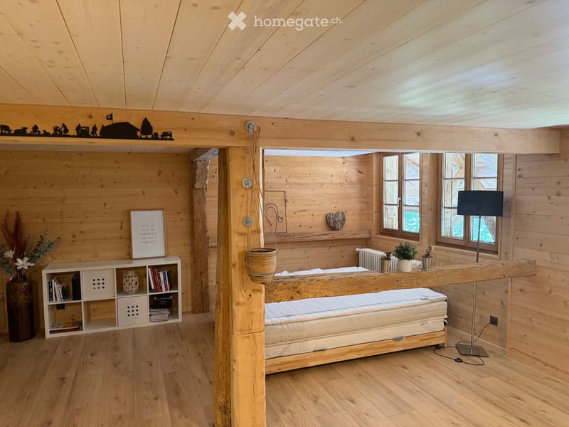 Cozy wooden bedroom with a large bed, wooden shelves, a hanging basket, and a floor lamp near the windows.