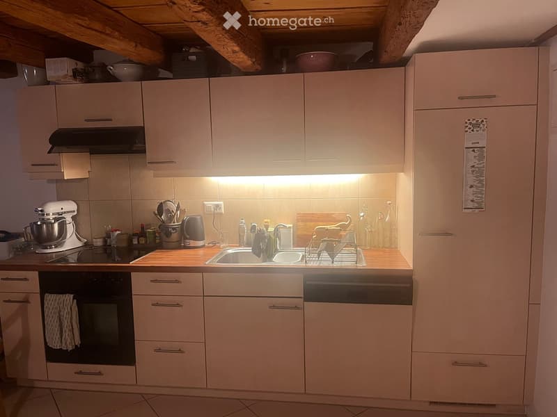 Modern kitchen with light-colored cabinets, stainless steel appliances, and a wooden countertop. Features include an oven, sink, dishwasher, mixer, and various kitchen utensils.