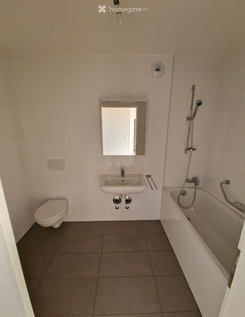 Modern bathroom with a toilet, sink, bathtub, and mirror. Light-colored tiles and a neutral color scheme.