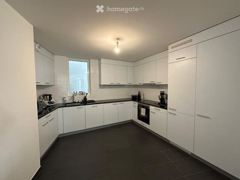 Modern kitchen with white cabinets, black countertops, and black tiled floor. Features a sink, oven, coffee maker, and microwave.