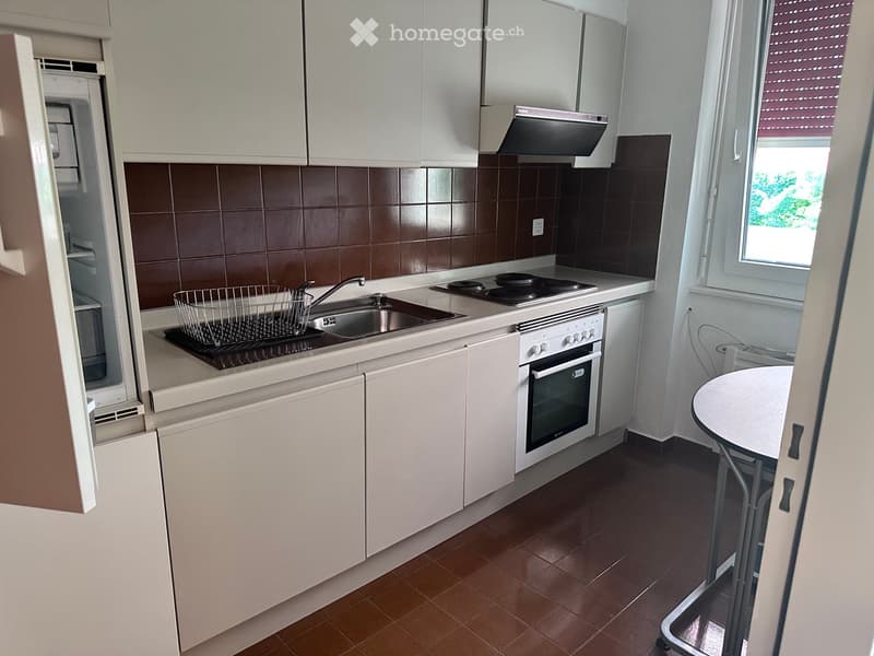Modern kitchen with white cabinets, stainless steel appliances, and a small round table near the window.