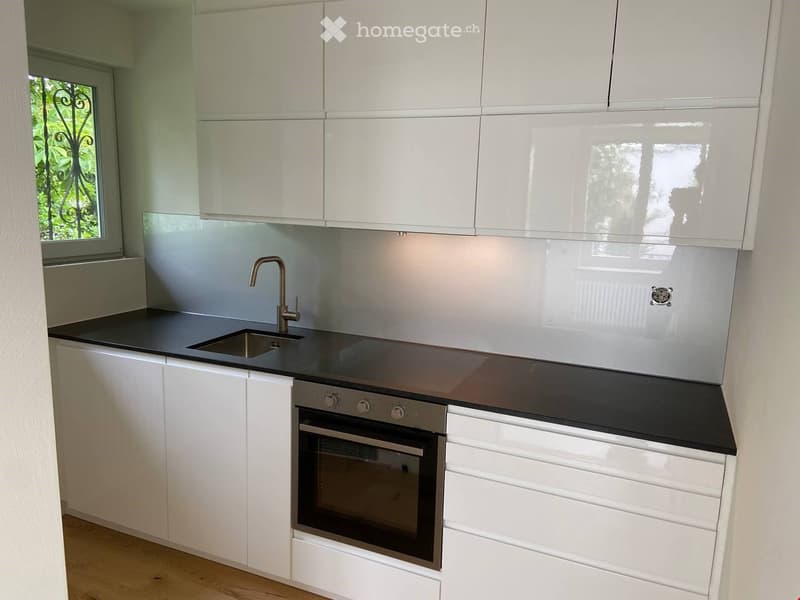 modern kitchen with white cabinets, black countertops, stainless steel sink, oven, and faucet, glass backsplash, wooden floor