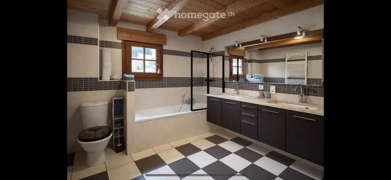 Modern bathroom with a checkered tile floor, dark grey cabinets, a bathtub, toilet, and a large mirror above the sink.