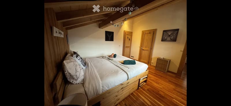 Cozy bedroom with wooden bed, pillows, blanket, wicker basket, and two picture frames on the wall.