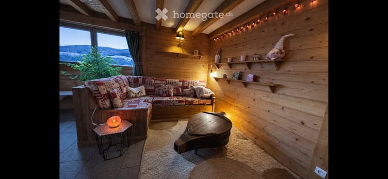 Cozy living room with wooden walls, exposed beams, large window with scenic view, plaid-patterned sofa, small coffee table, and decorative shelves.