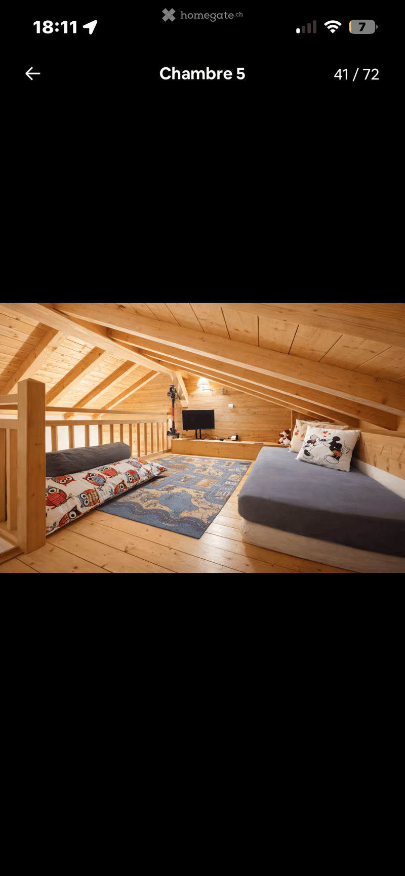 Cozy attic bedroom with wooden beams, a double bed, a sofa, a television, and a colorful rug.