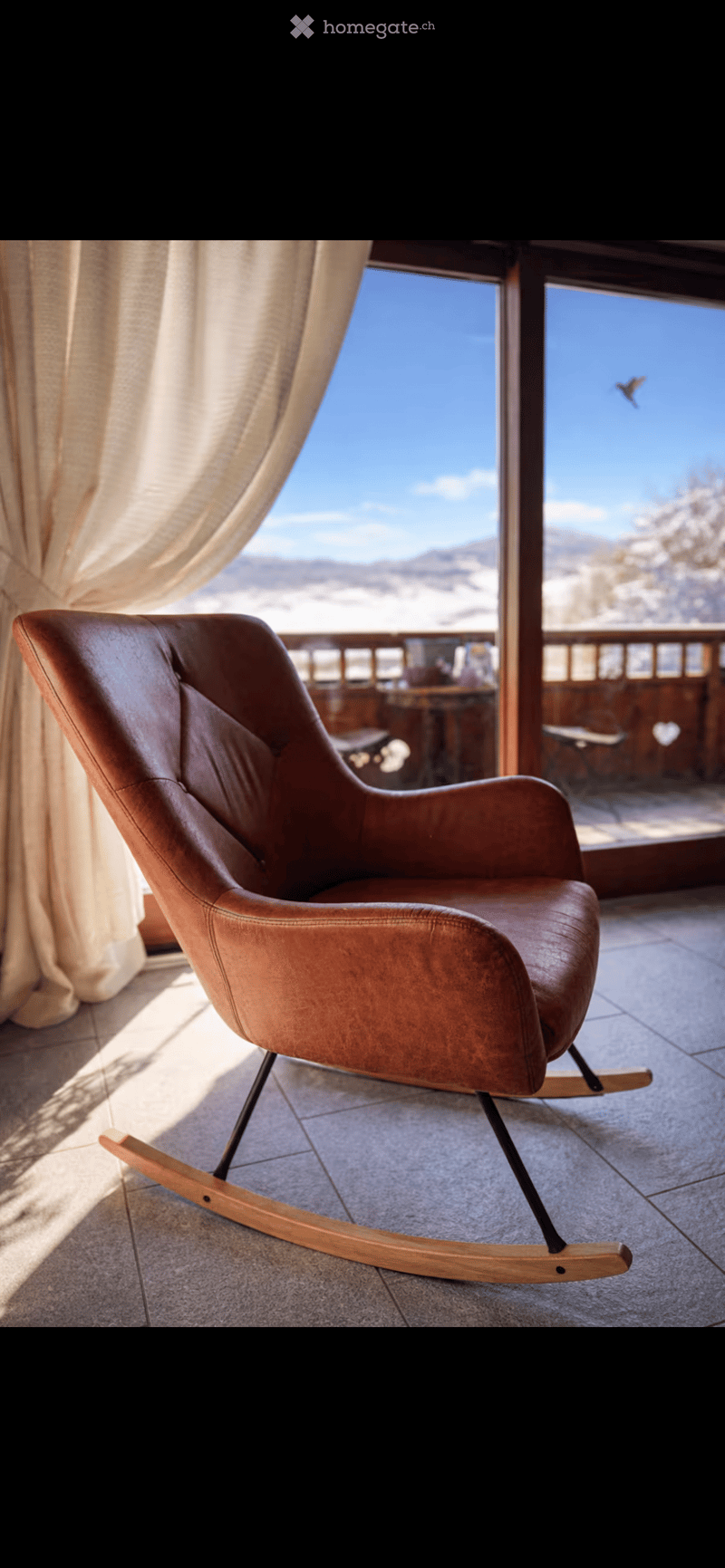 A modern leather rocking chair with wooden base is placed near a large window with a scenic mountain view.