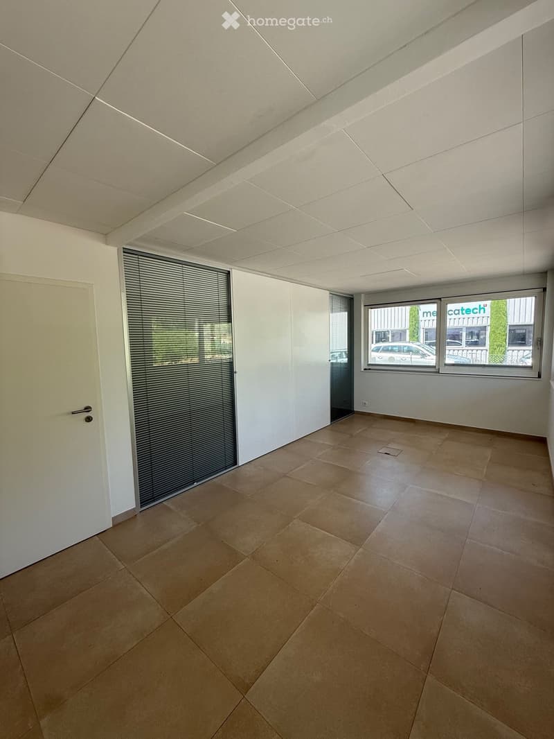 Empty room with beige tiled floor, white walls, large windows with blinds, and a white door.