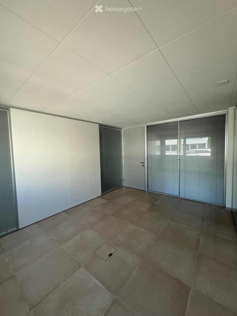 Empty room with tiled floor, white walls, large windows with blinds, and a door.