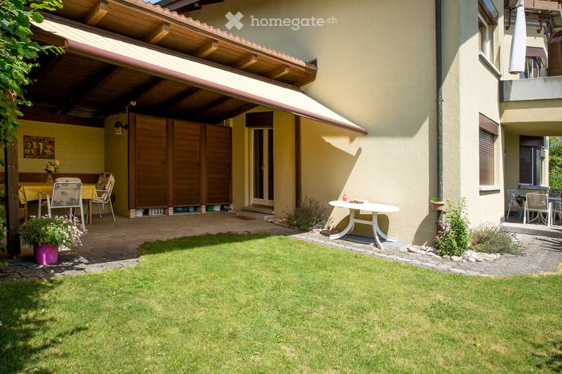 Well-maintained garden with a lawn, patio area, outdoor furniture, and covered seating area with a table and chairs.