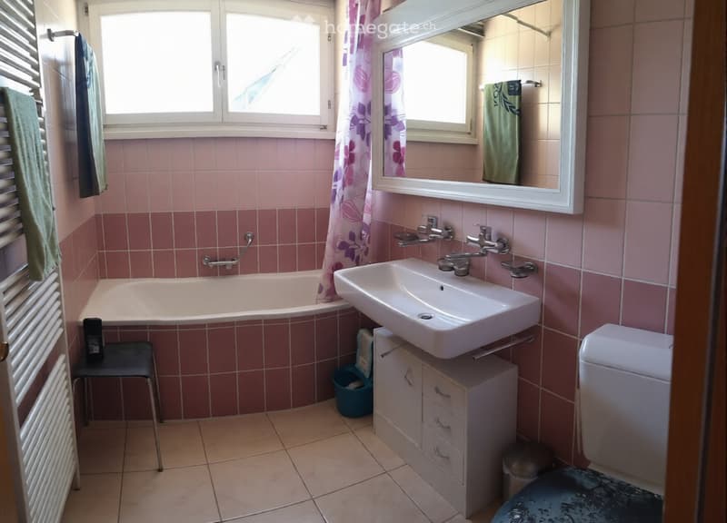 Bathroom with pink tiles, bathtub, sink, toilet, cabinet, mirror, and towels.