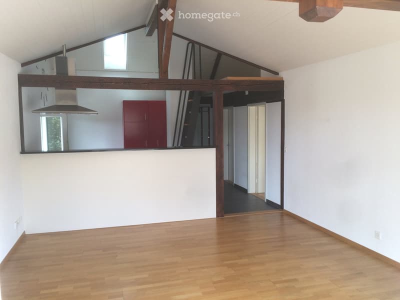 Empty room with wooden flooring, white walls, and exposed wooden beams. A raised platform with a red cabinet and a range hood is visible in the background.