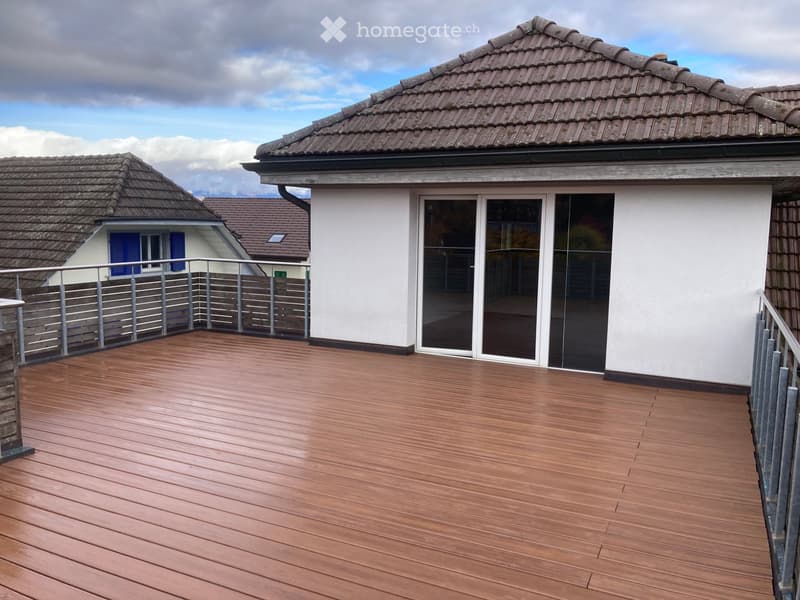 Wooden deck with metal railings, large sliding glass doors, and a view of neighboring houses and a tiled roof.