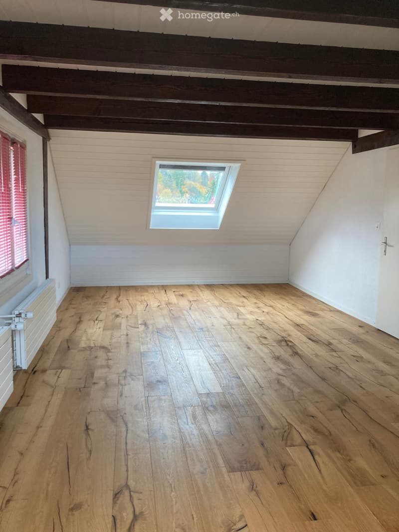 Empty attic room with wooden floors, white walls, exposed wooden beams, and a skylight window.