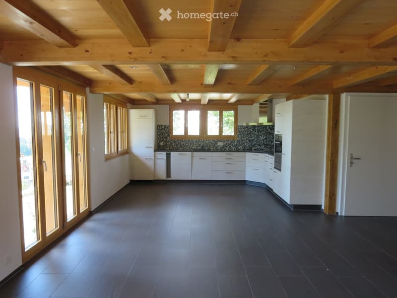 Modern kitchen with white cabinets, dark tiled floor, and exposed wooden beams on the ceiling. Features a central island with sink and oven, and large windows with wooden frames.