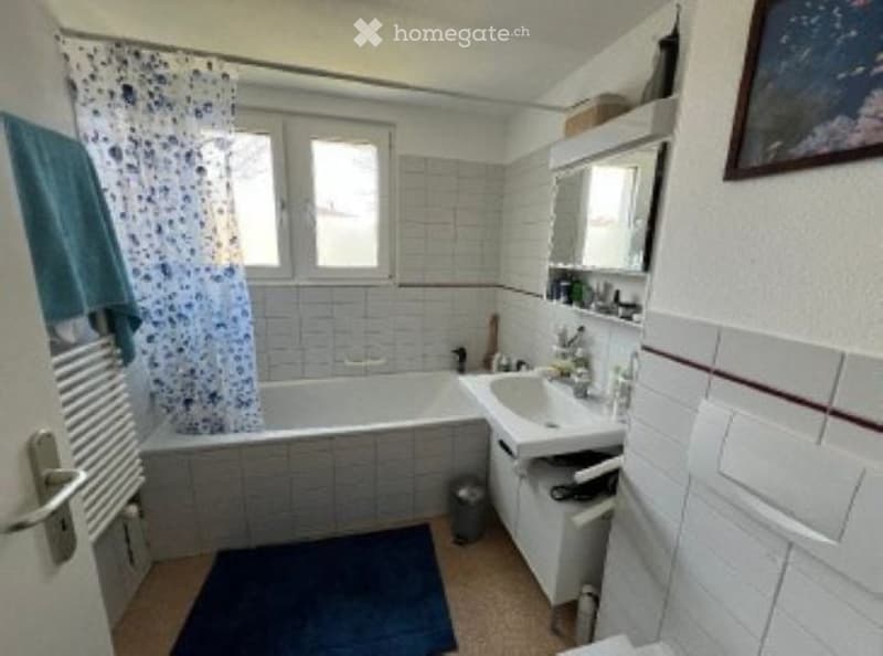 Bathroom with a bathtub, sink, mirror, shower curtain, and a towel on the floor.
