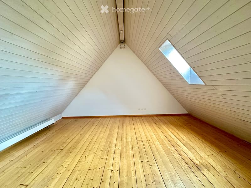 Empty room with wooden flooring, white walls, and a slanted wooden ceiling with a small skylight window.