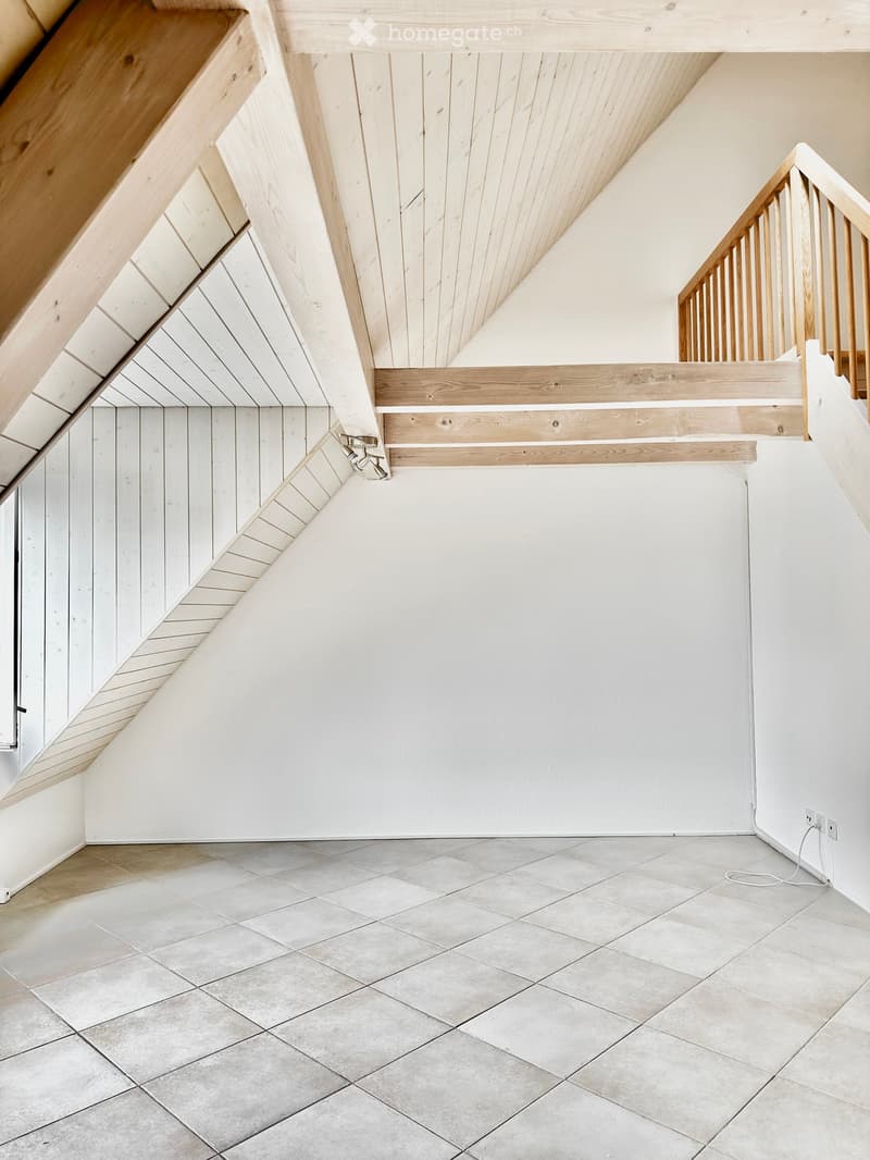 Modern hallway with a wooden staircase, white walls, and tiled floor. The staircase features a wooden railing and steps, with a slanted ceiling and built-in lighting.