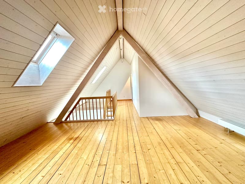 Empty attic space with wooden floors, slanted wooden ceilings, and skylights, featuring a wooden staircase leading downwards.