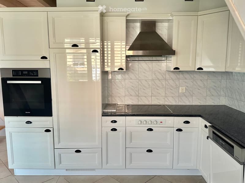 Modern kitchen with white cabinets, stainless steel appliances, and marble backsplash.