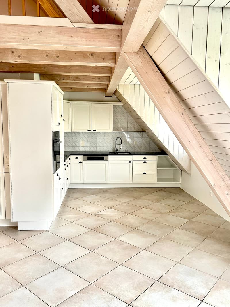 Modern kitchen with white cabinets, stainless steel appliances, and a tiled floor. The ceiling has exposed wooden beams and slanted design.