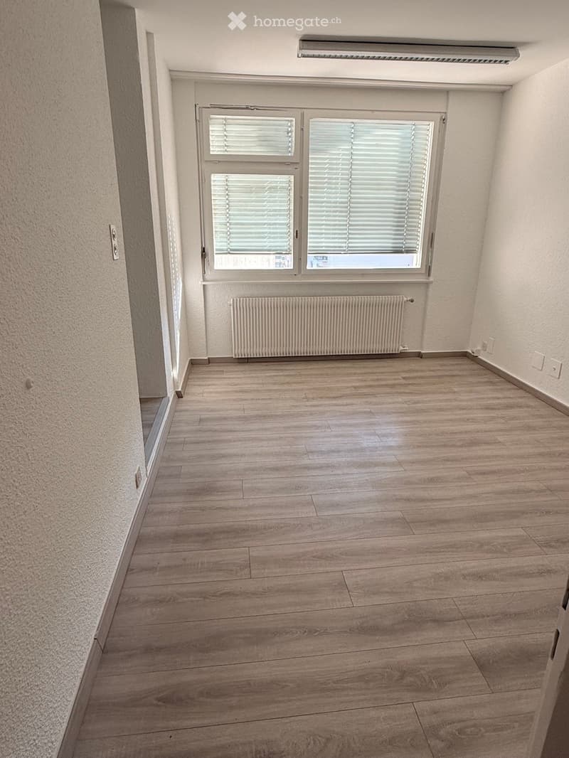 Empty room with wooden flooring, white walls, and a window with blinds. A radiator is placed below the window.