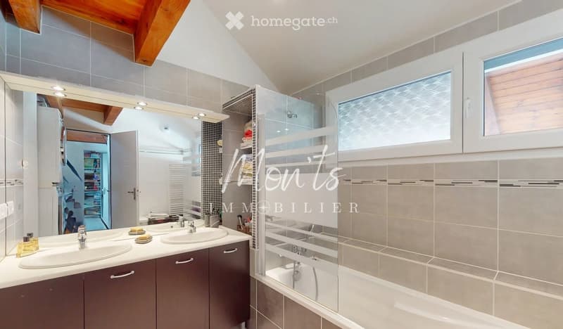 Modern bathroom with double sink vanity, large mirror, bathtub, and built-in cabinets. Features a sleek design with grey tiles and wooden accents.