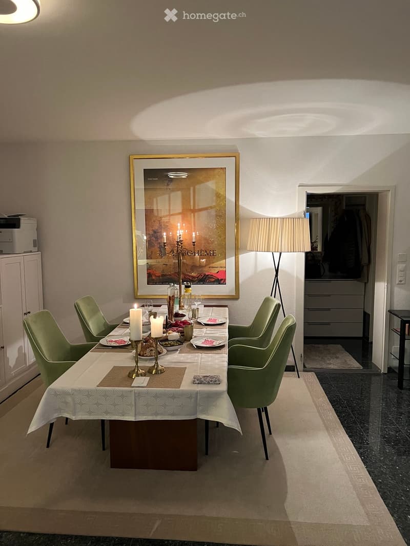 Dining room with a round table set for a meal, surrounded by green chairs, a floor lamp, and a framed picture on the wall.