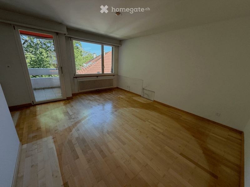 Empty room with wooden flooring, large windows, and a sliding door leading to a balcony.